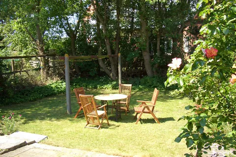 Sichtgeschützter Garten des Vormannshuus mit Rasen, Gartentisch und Holzstühlen unter Bäumen