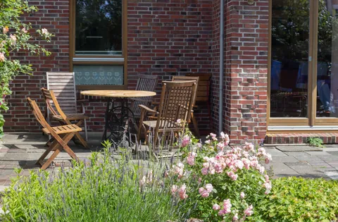 Terrasse des Vormannshuus mit Holztisch und Klappstühlen vor der Klinkerwand, davor Lavendel und Rosen
