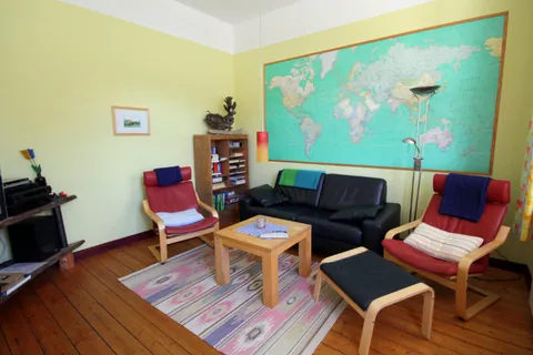 Wohnzimmer im Vormannshuus mit schwarzem Ledersofa, zwei roten Sesseln, Couchtisch und großer Weltkarte an der Wand