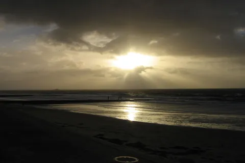 Abendsonne bricht durch dunkle Wolken über dem Strand von Borkum